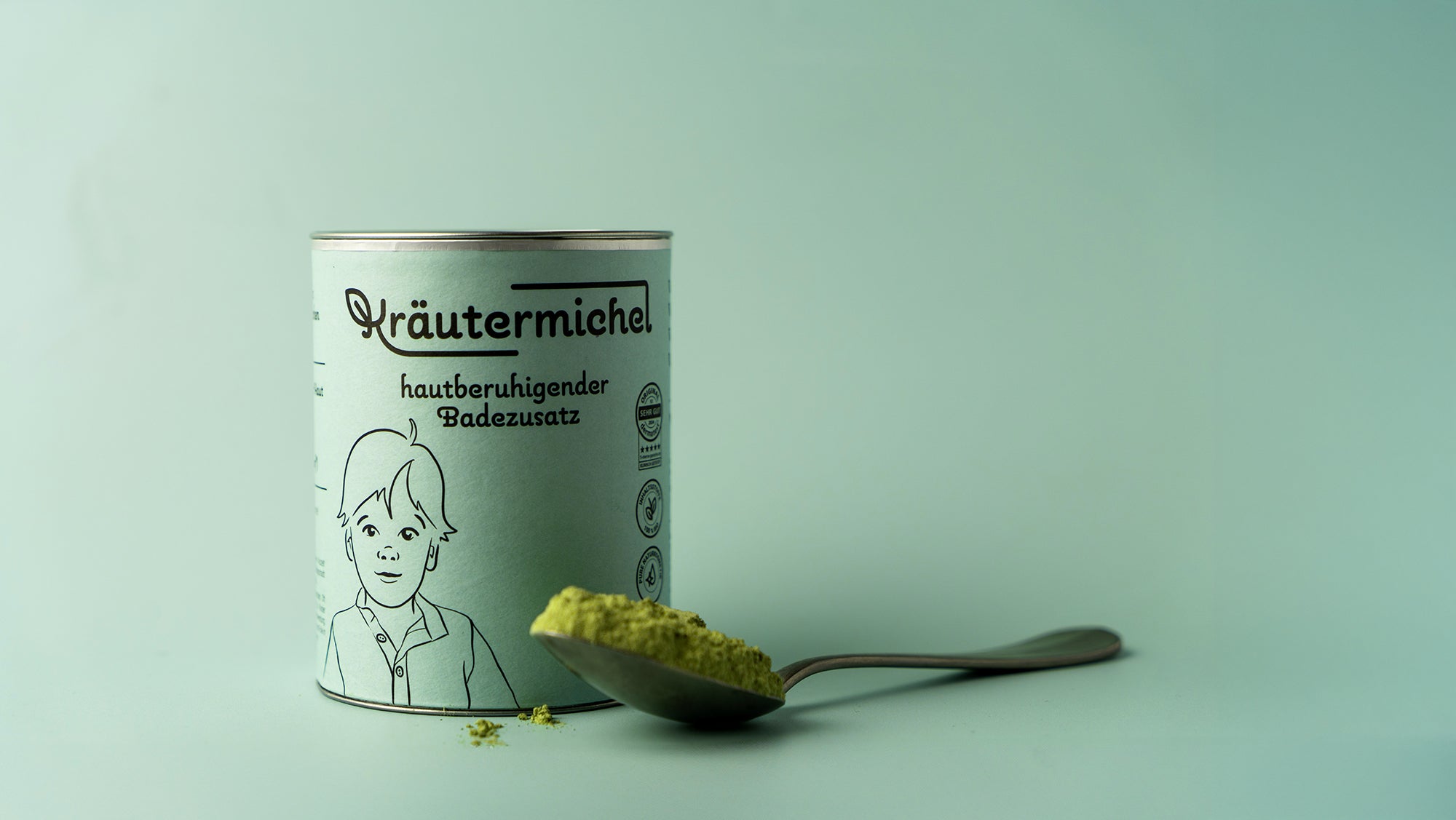 Kräutermichel Badezusatz in nachhaltiger grüner Dose mit silbernem Deckel. Auf einem Löffel daneben ist der grüne, pulverförmige Badezusatz aus Bio-Inhaltsstoffen zu sehen.